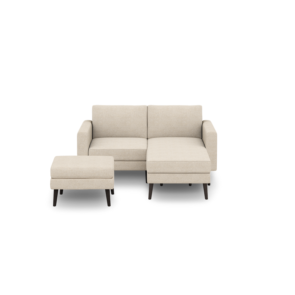 Beige modern sectional sofa with chaise lounge on right side and matching ottoman, both with dark wooden legs.