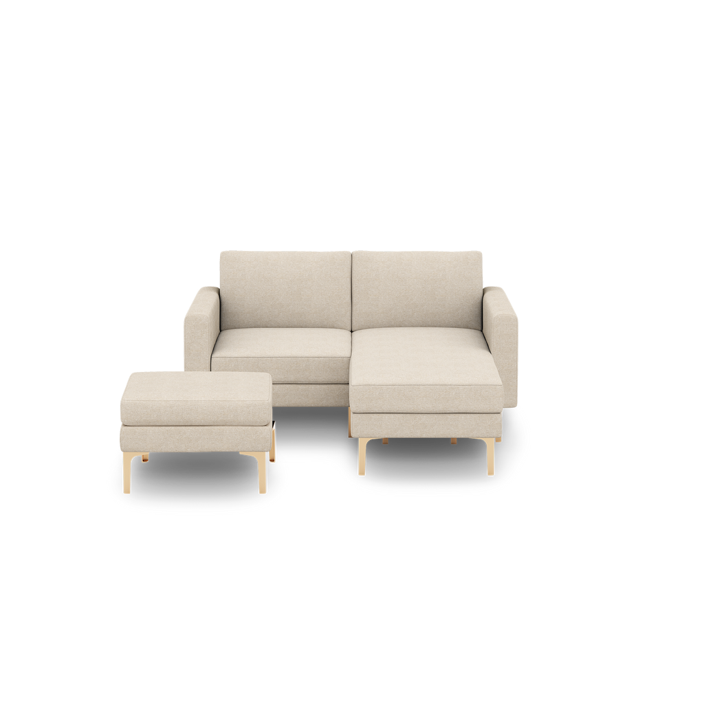 Beige fabric sectional sofa with chaise lounge on the right and matching ottoman, featuring light wooden legs.