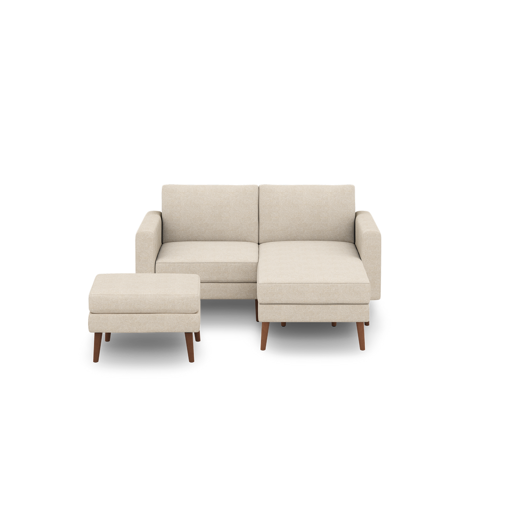Compact beige upholstered sectional sofa with wooden legs and a matching ottoman, designed for small living spaces.