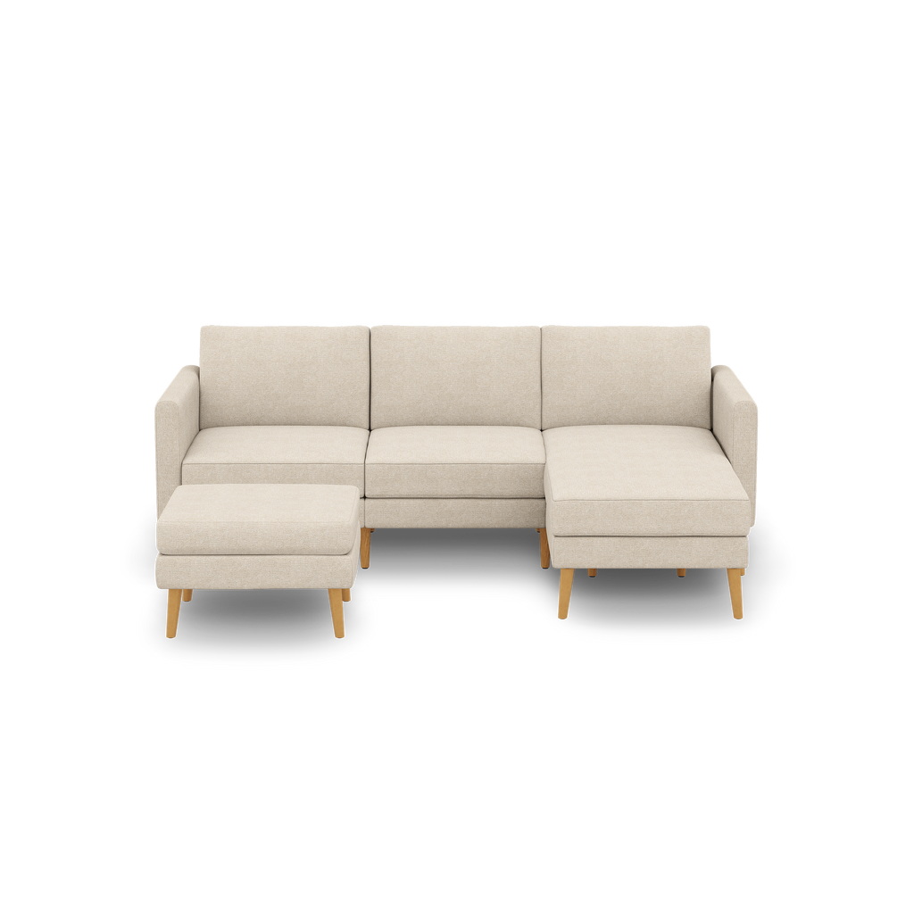 Beige fabric sectional sofa with a left-side ottoman and right-side chaise, supported by light wooden legs.