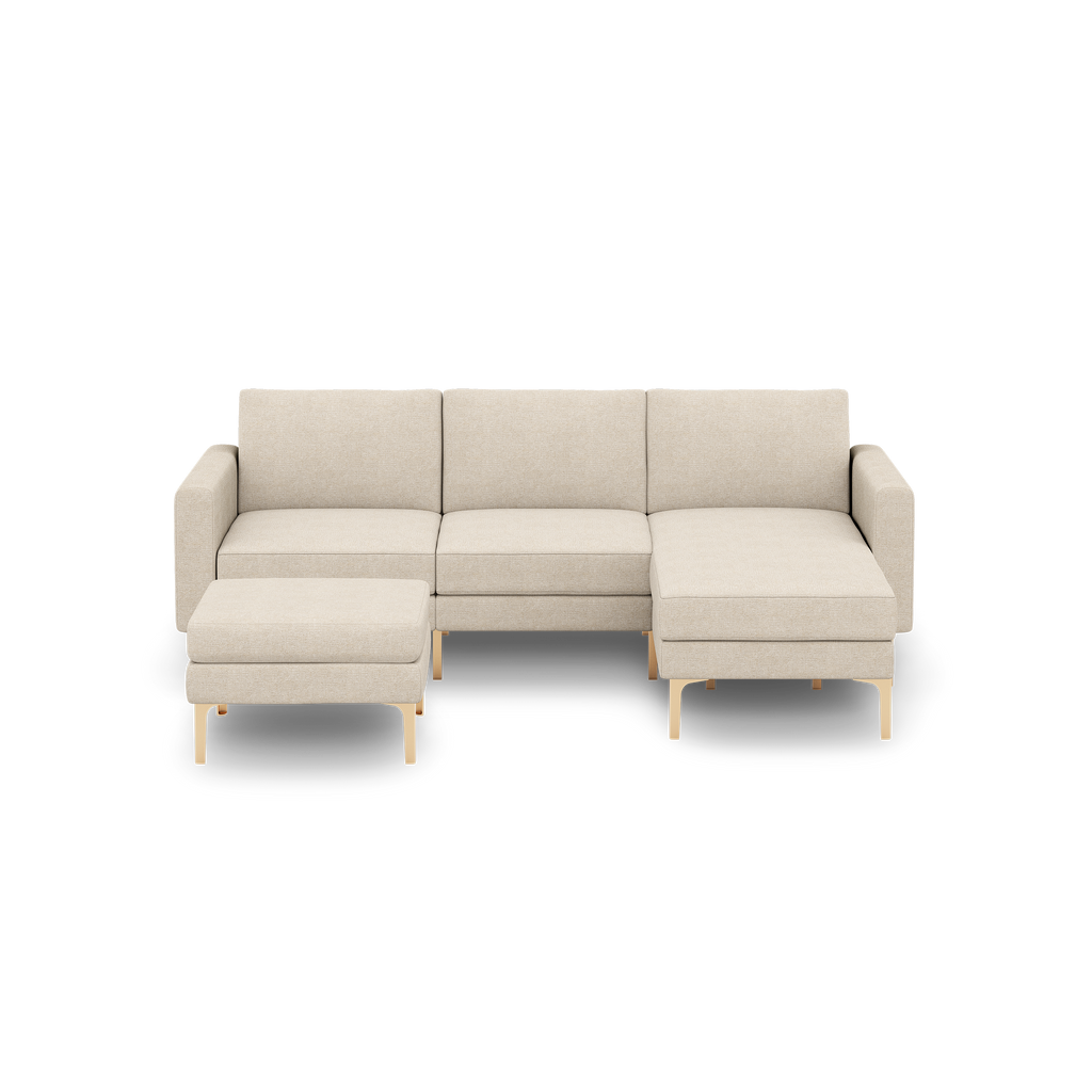 Beige three-seater sectional sofa with chaise lounge and matching ottoman, wooden legs, modern minimalist design.