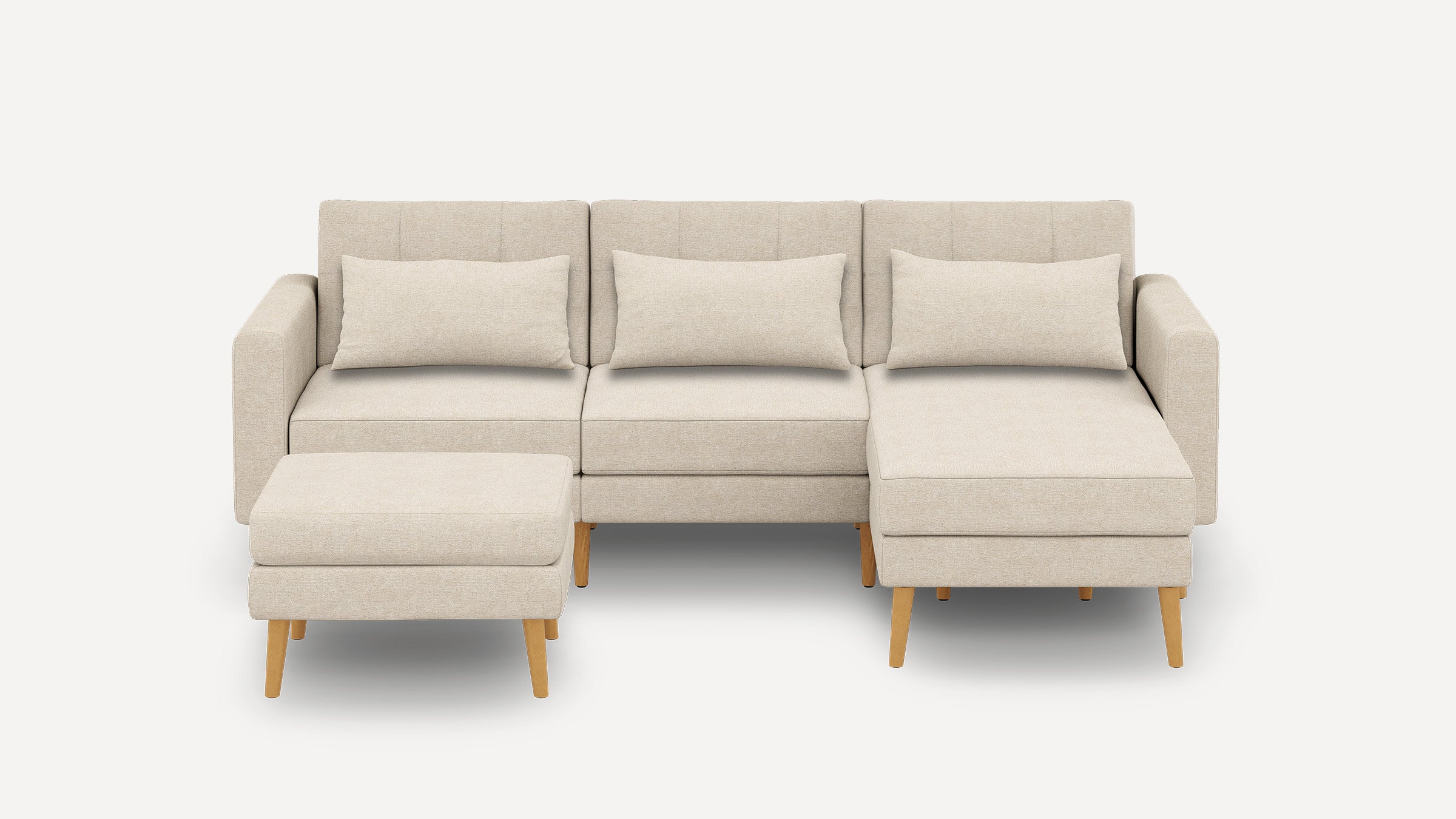 Beige fabric sectional sofa with three back cushions, wooden legs, and a matching ottoman on a white background.