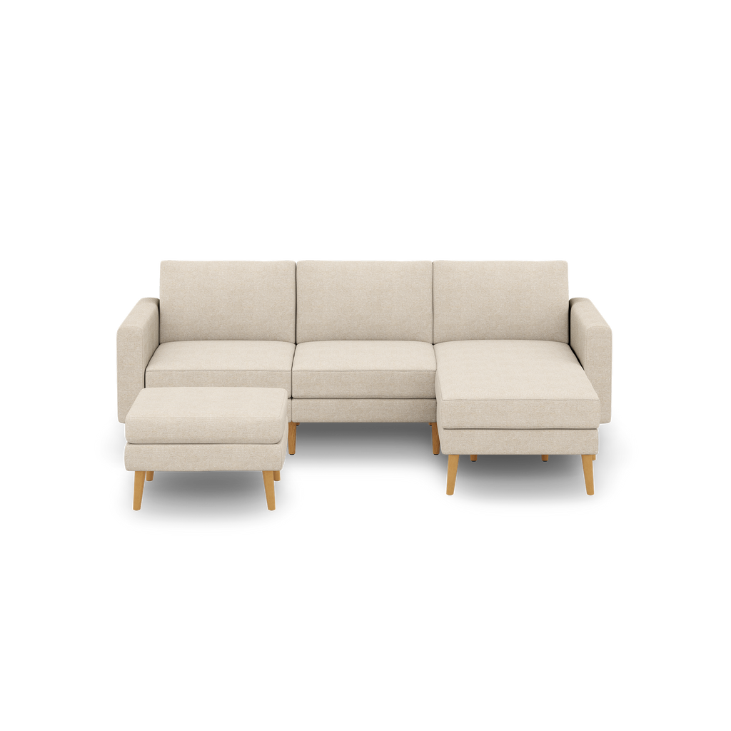 Beige fabric sectional sofa with wooden legs, featuring three seat cushions and a matching ottoman on left side.