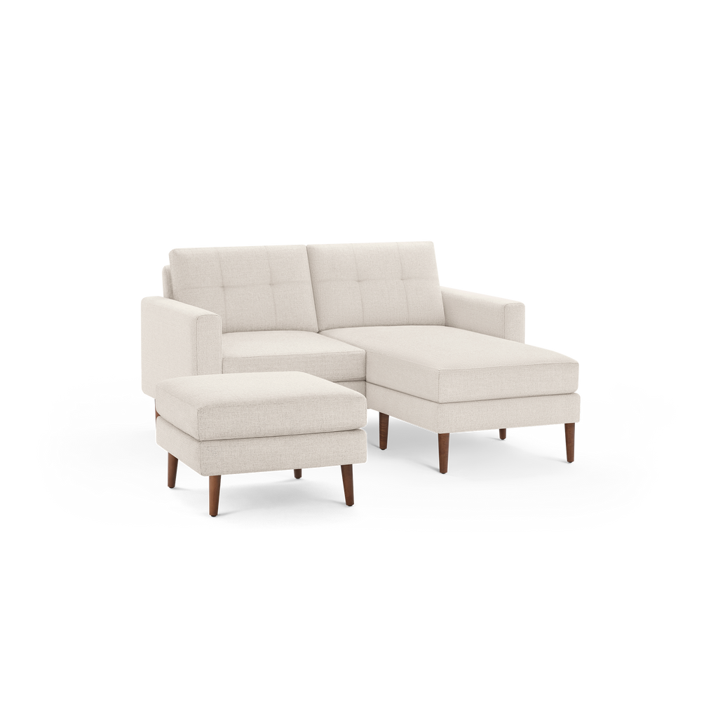 Beige fabric sectional sofa with tufted back cushions, straight arms, wooden legs, and a matching ottoman.