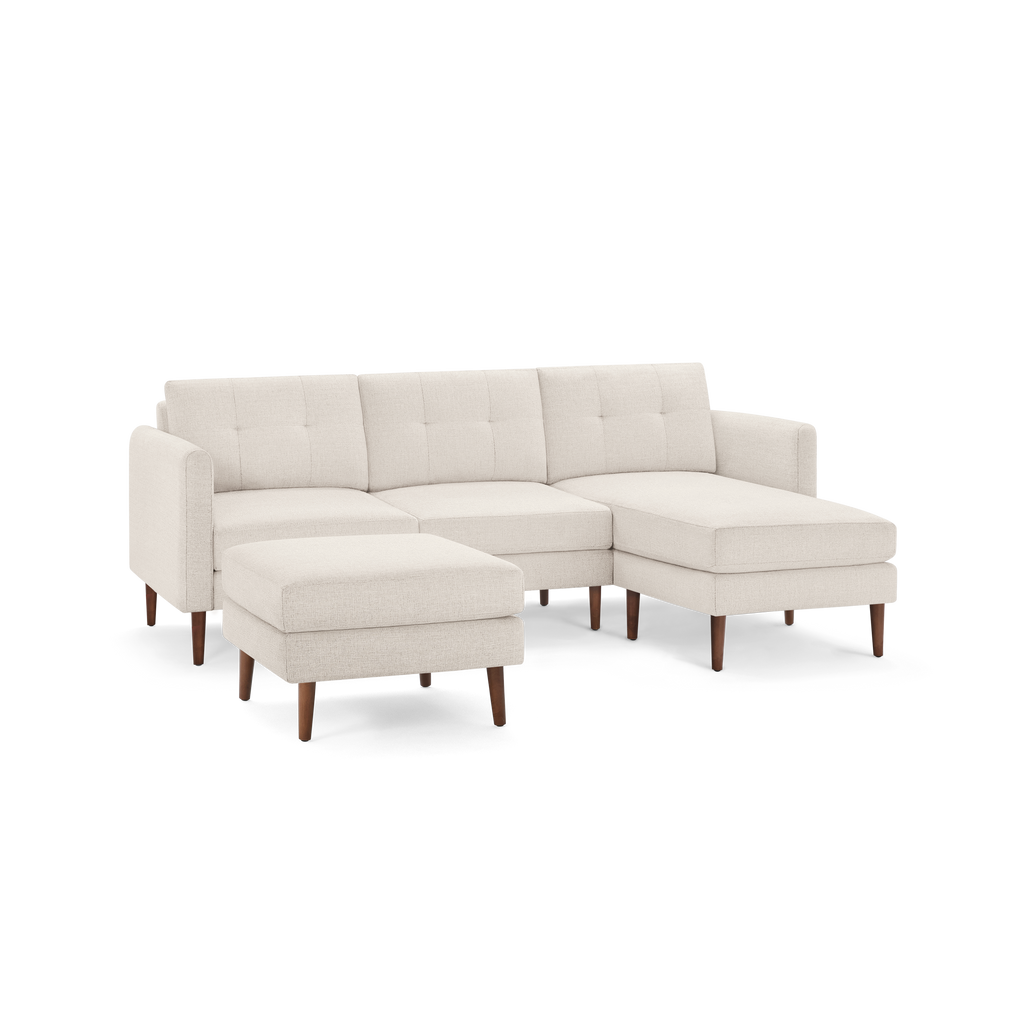 Cream-colored modern sectional sofa with tufted cushions, wooden legs, and a matching ottoman, L-shaped design.