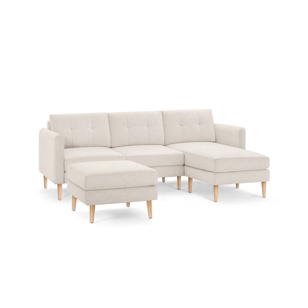 Light beige modern sectional sofa with tufted back cushions, wooden legs, and separate ottoman against transparent background.
