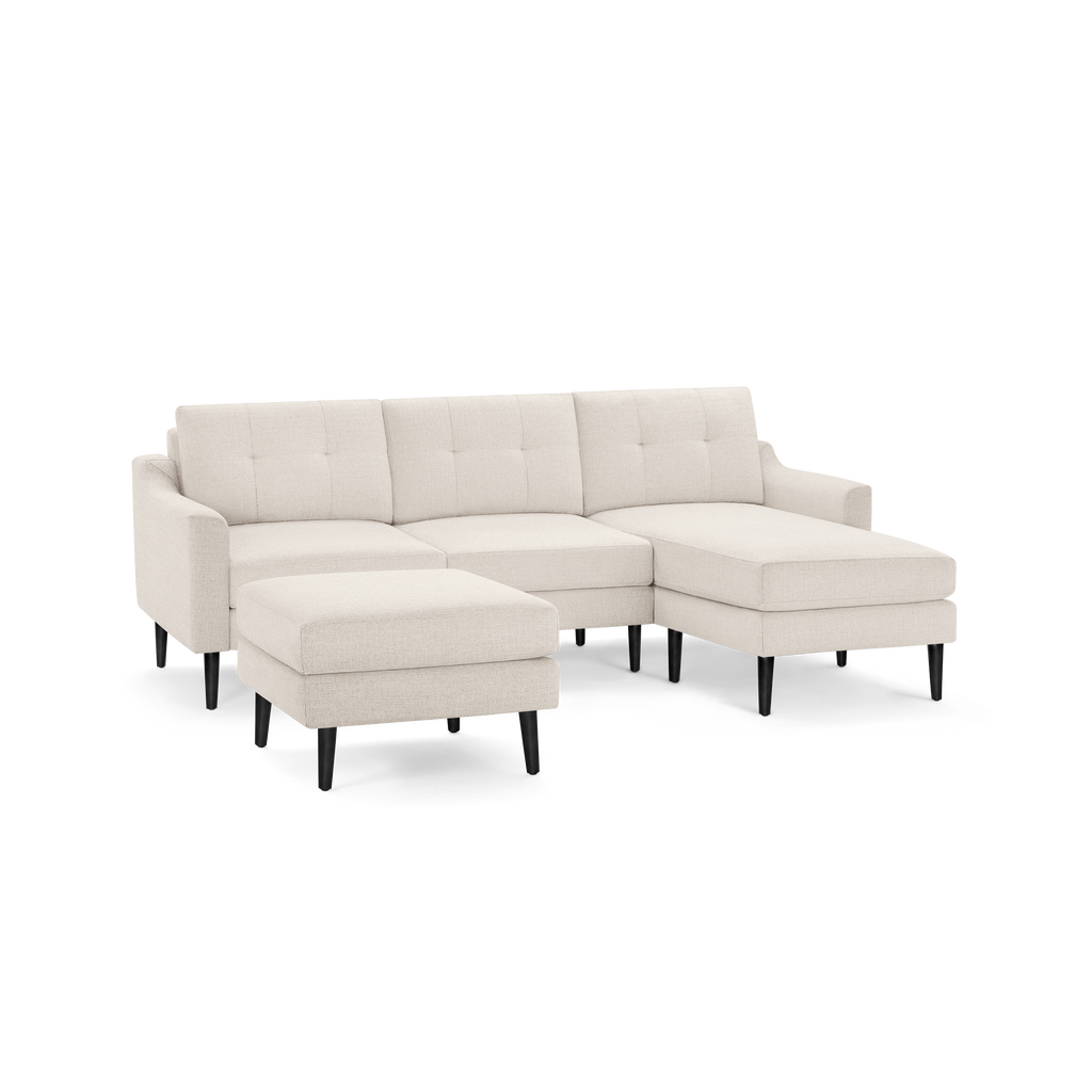 Beige fabric sectional sofa with tufted back cushions, left chaise, and separate ottoman on black wooden legs.