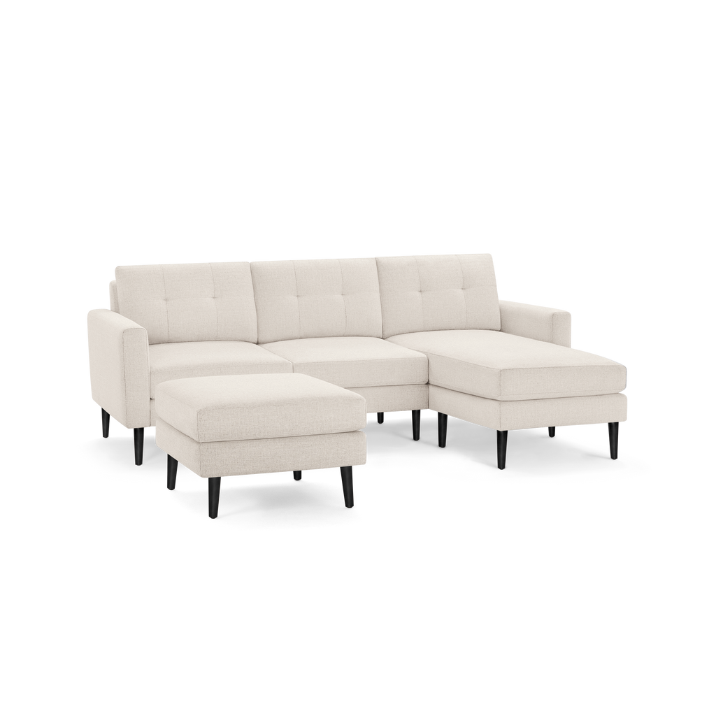 Modern beige sectional sofa with tufted back cushions, sleek black tapered legs, and matching ottoman.