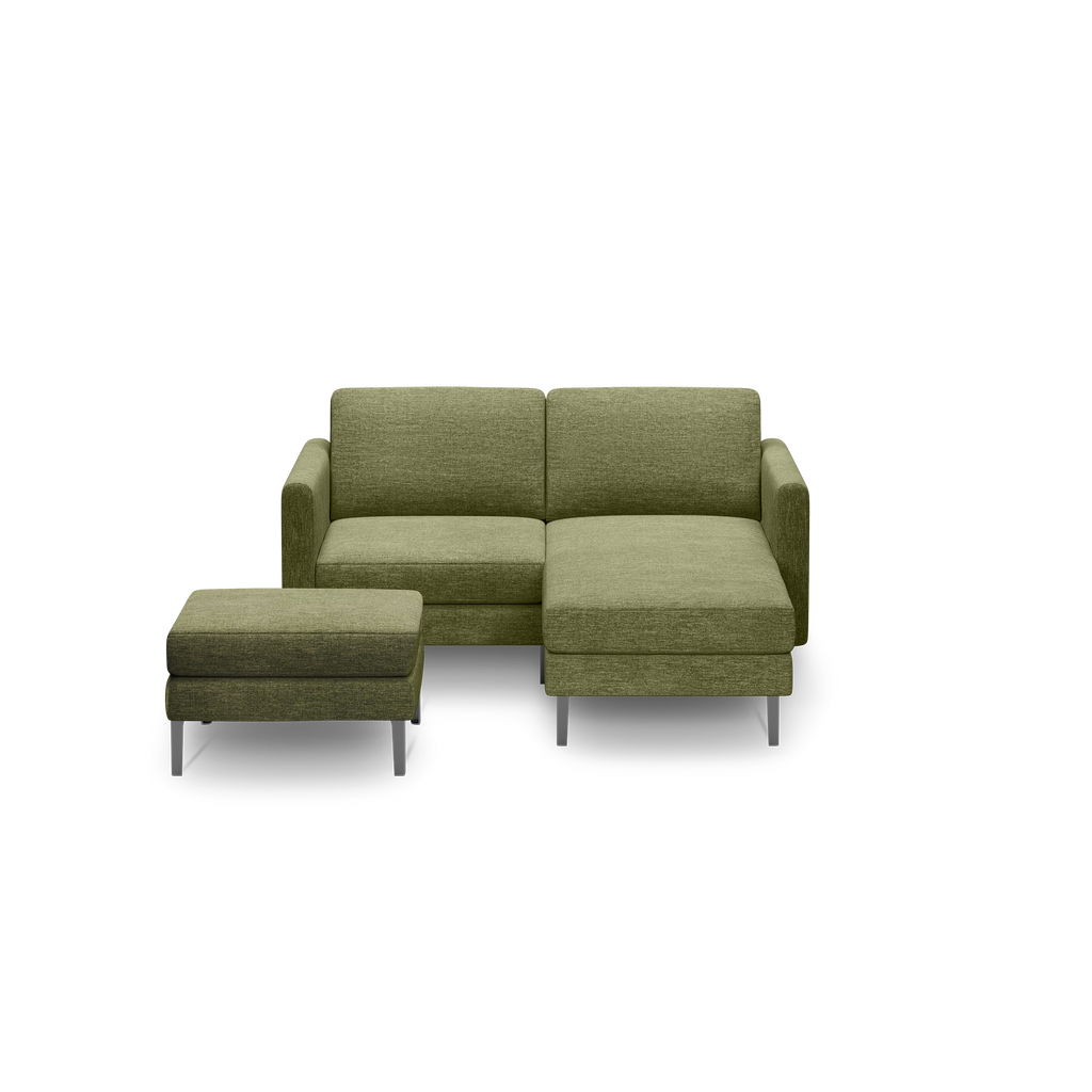 Green upholstered sectional sofa with chaise and matching ottoman on silver metal legs, against black background.
