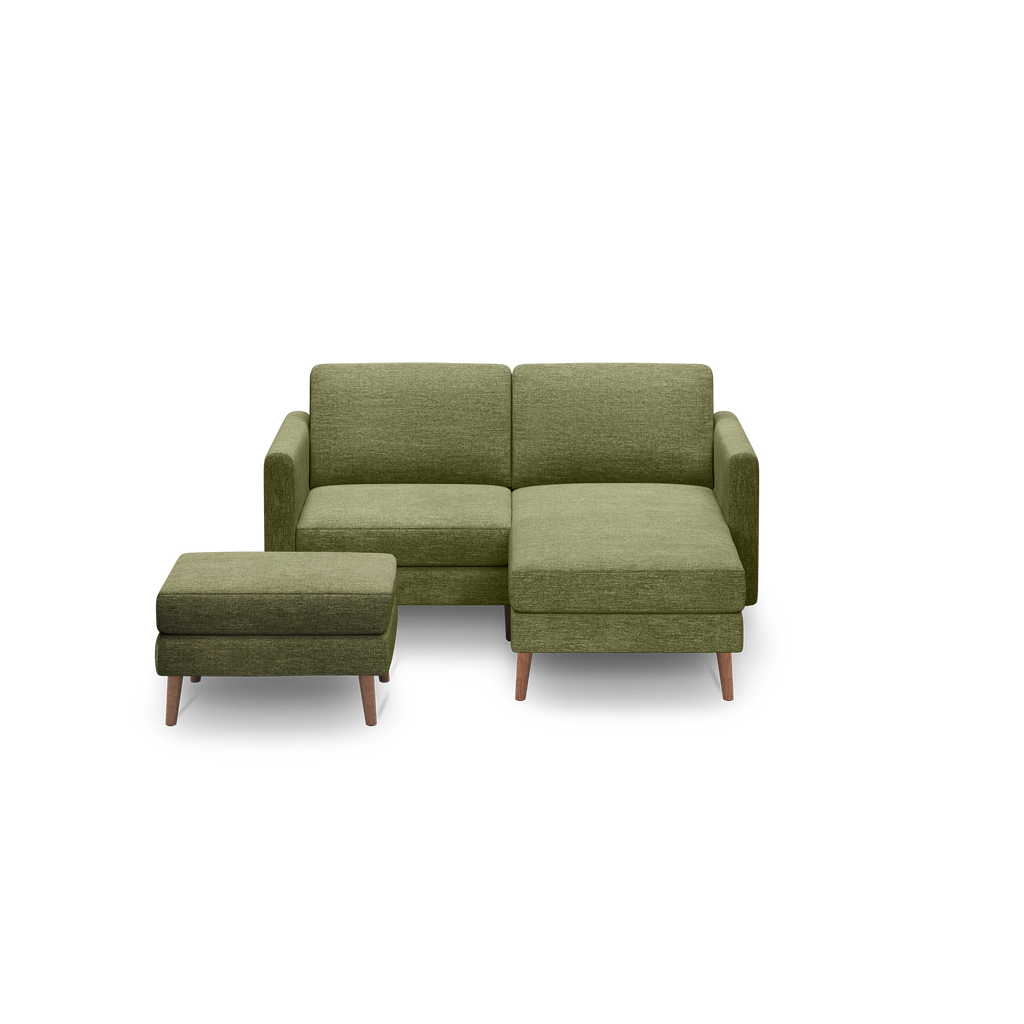 Green L-shaped fabric sofa with wooden legs and a matching green ottoman against a black background.