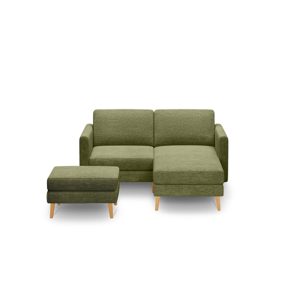 Modern olive green fabric sectional sofa with wooden legs and matching square ottoman on black background.