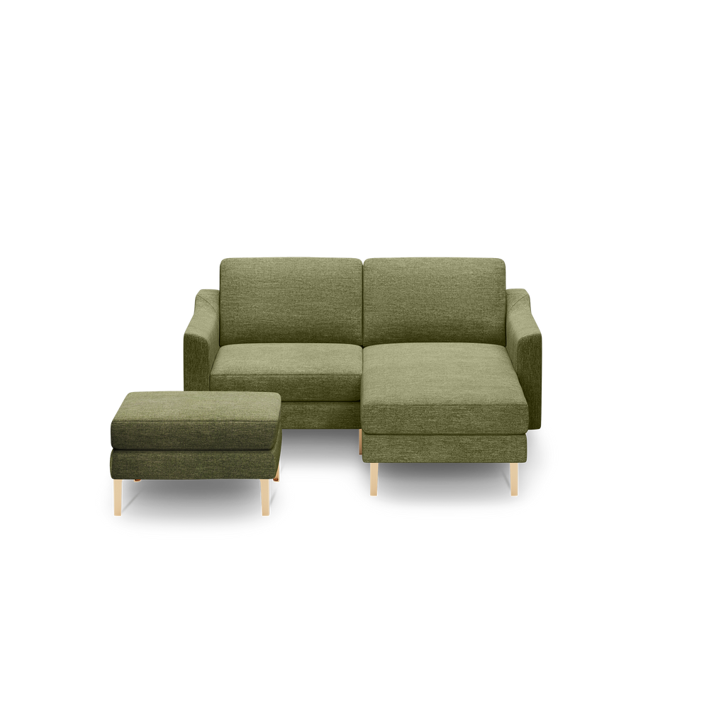 Green fabric L-shaped sectional sofa with matching ottoman, supported by light wooden legs, shown on black background.