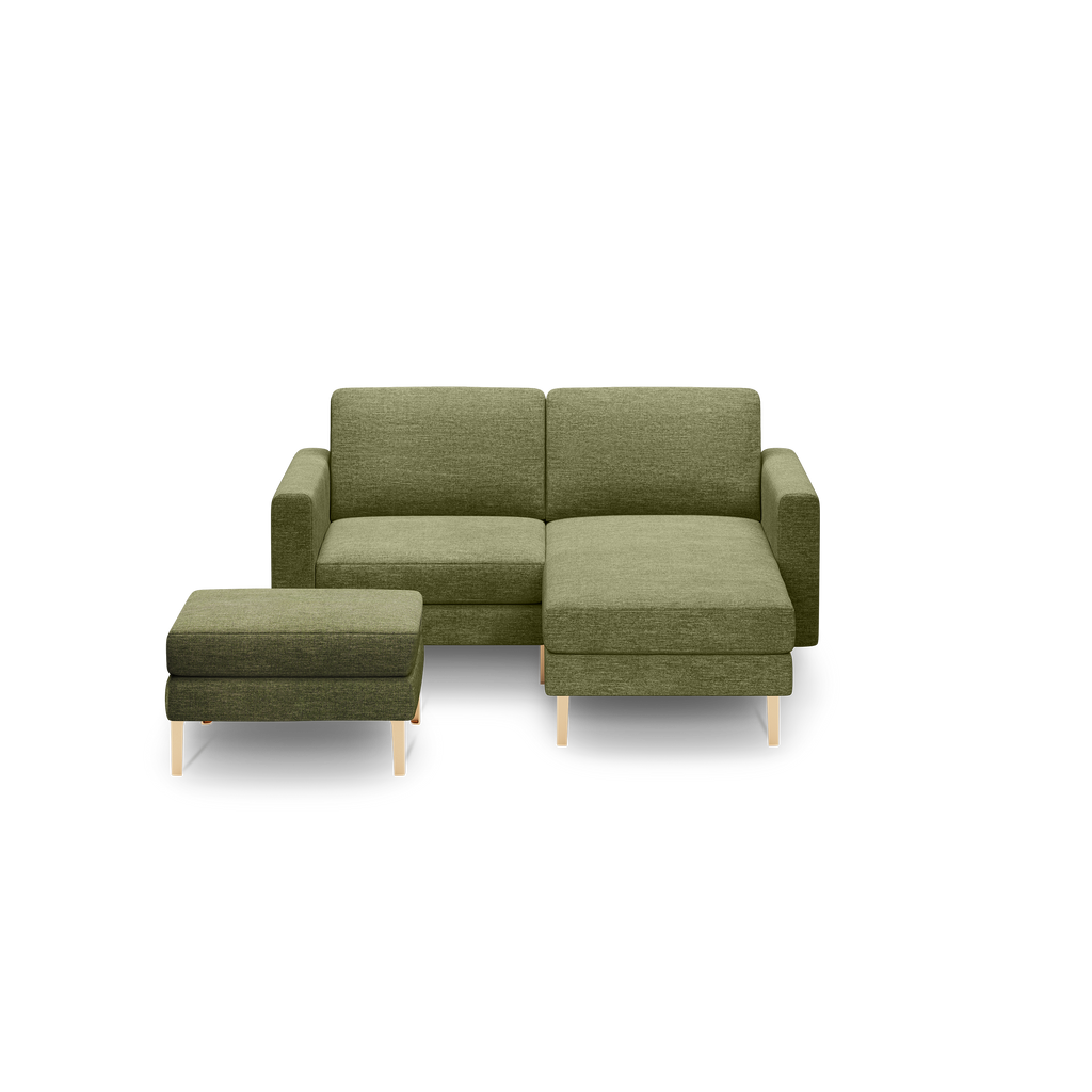 Modern olive green fabric sectional sofa with chaise and matching ottoman on light wooden legs, isolated on black background.