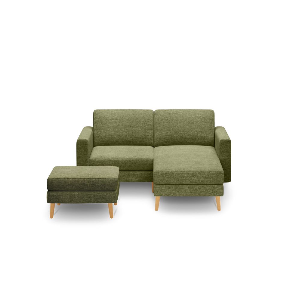 Modern olive green fabric sofa with wooden legs, featuring a chaise lounge and matching ottoman on a black background.