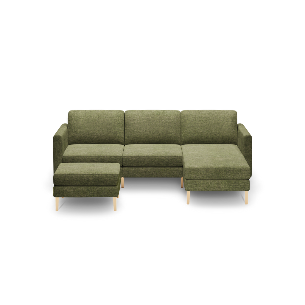 Olive green fabric sectional sofa with a chaise lounge on the right and a matching ottoman, both featuring light wooden legs.
