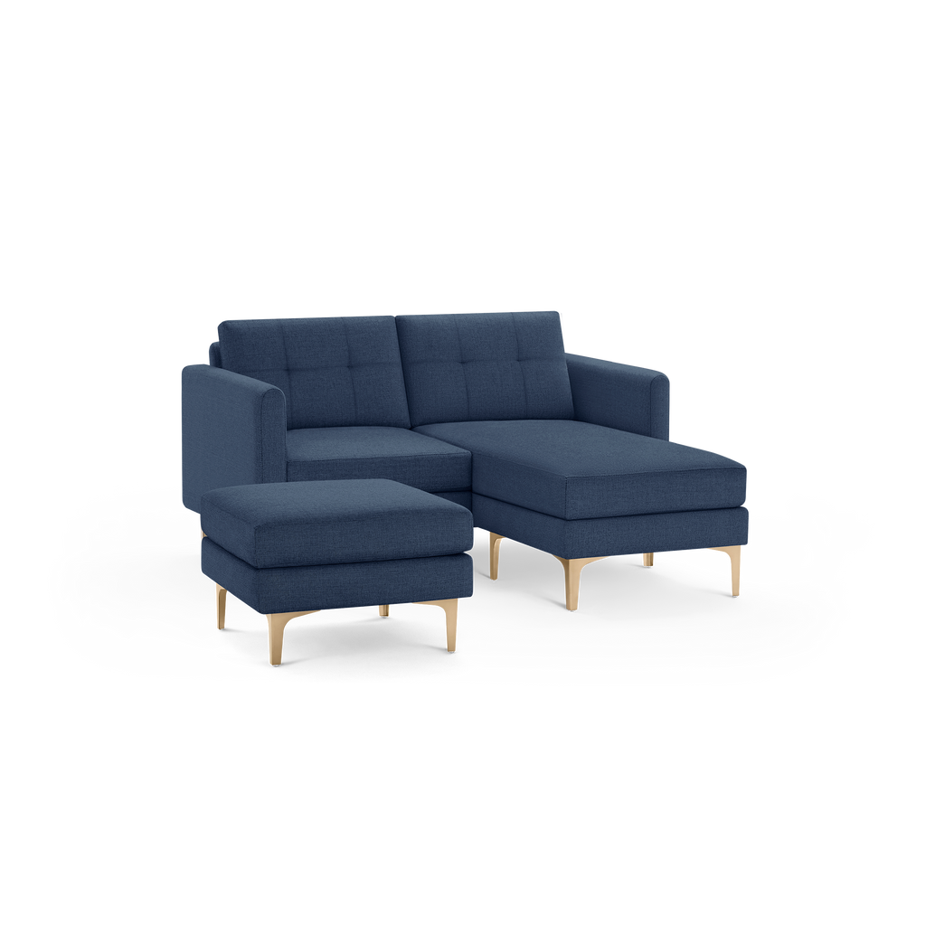 Modern navy blue fabric sectional sofa with tufted back cushions, chaise lounge, matching ottoman, and gold metal legs.