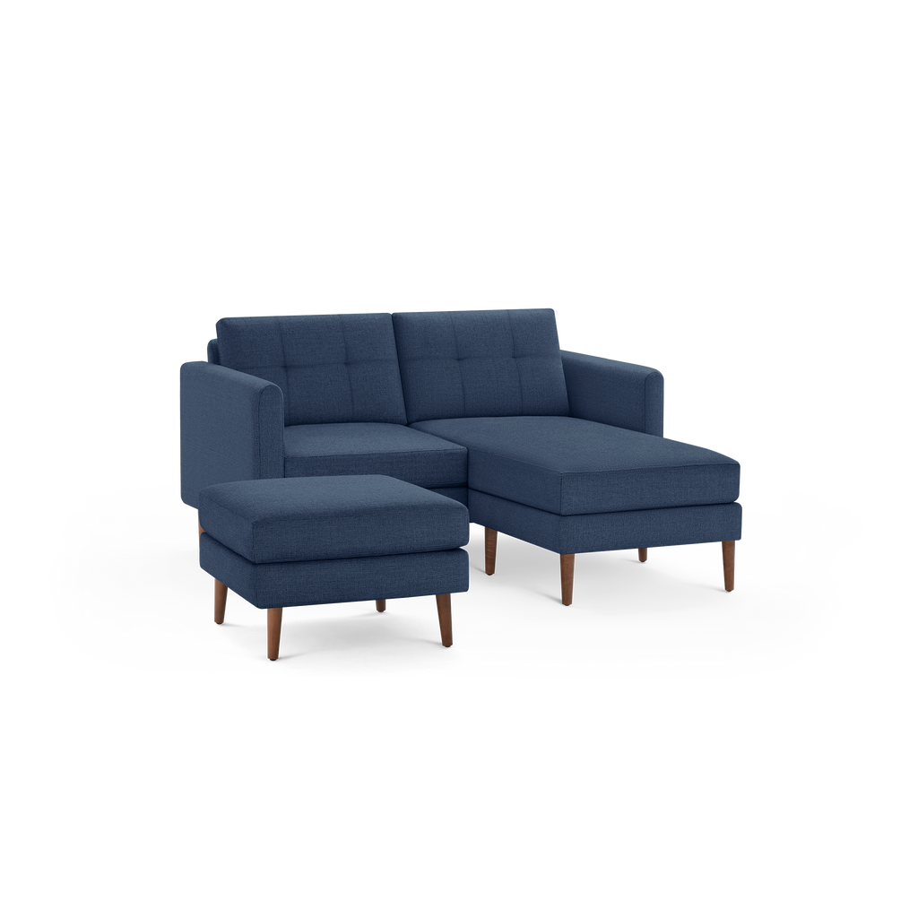 Modern navy blue fabric sectional sofa with tufted cushions and matching ottoman on wooden legs, isolated on black background.