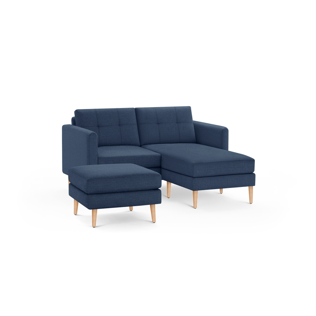 Modern navy blue fabric sectional sofa with tufted back cushions and light wooden legs, including a matching ottoman.