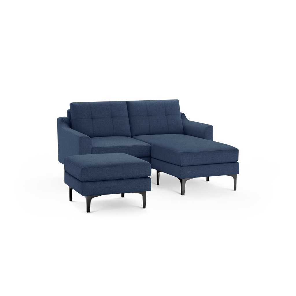 Modern navy blue sectional sofa with tufted back cushions, metal legs, and matching ottoman, isolated on black background.