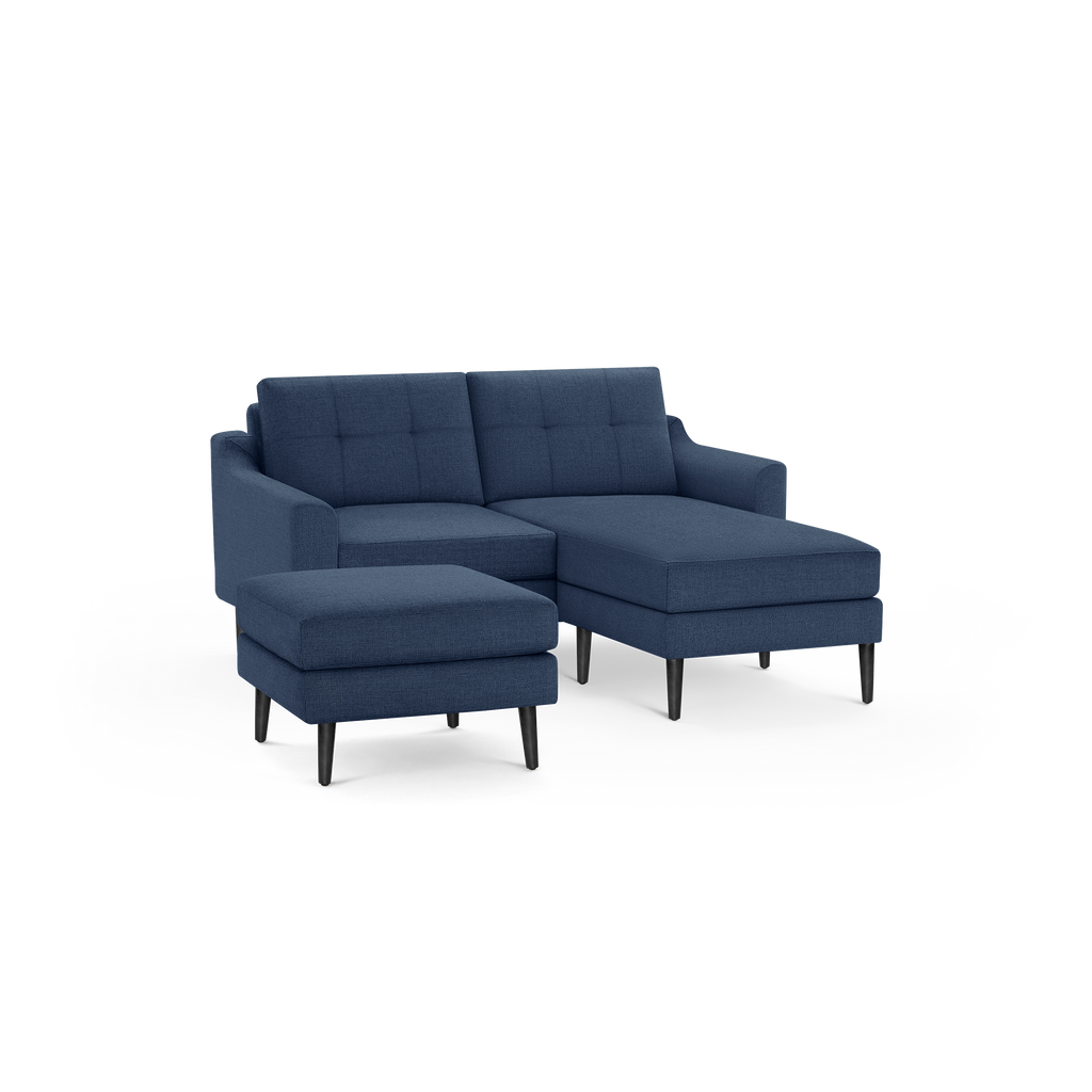 Modern navy blue fabric sectional sofa with tufted back cushions and matching ottoman on black wooden legs.