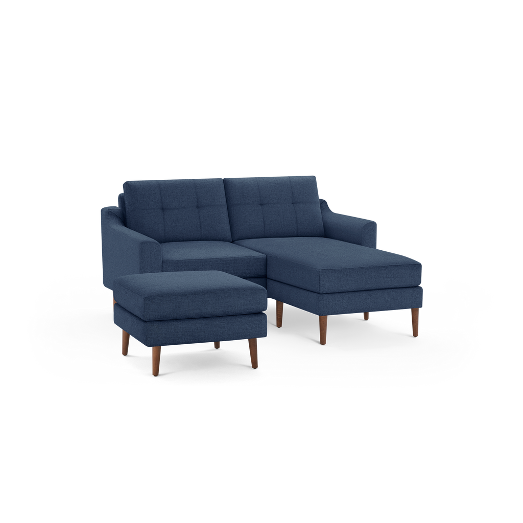 Mid-century modern navy blue fabric sectional sofa with tufted back cushions and wooden tapered legs, accompanied by a matching ottoman.