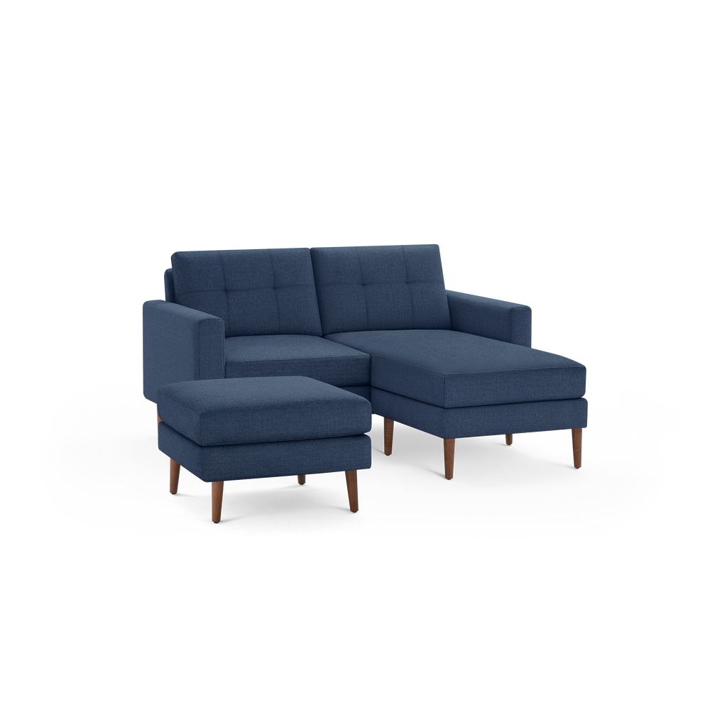 Modern navy blue upholstered sectional sofa with matching ottoman, tufted back cushions, and wooden legs.