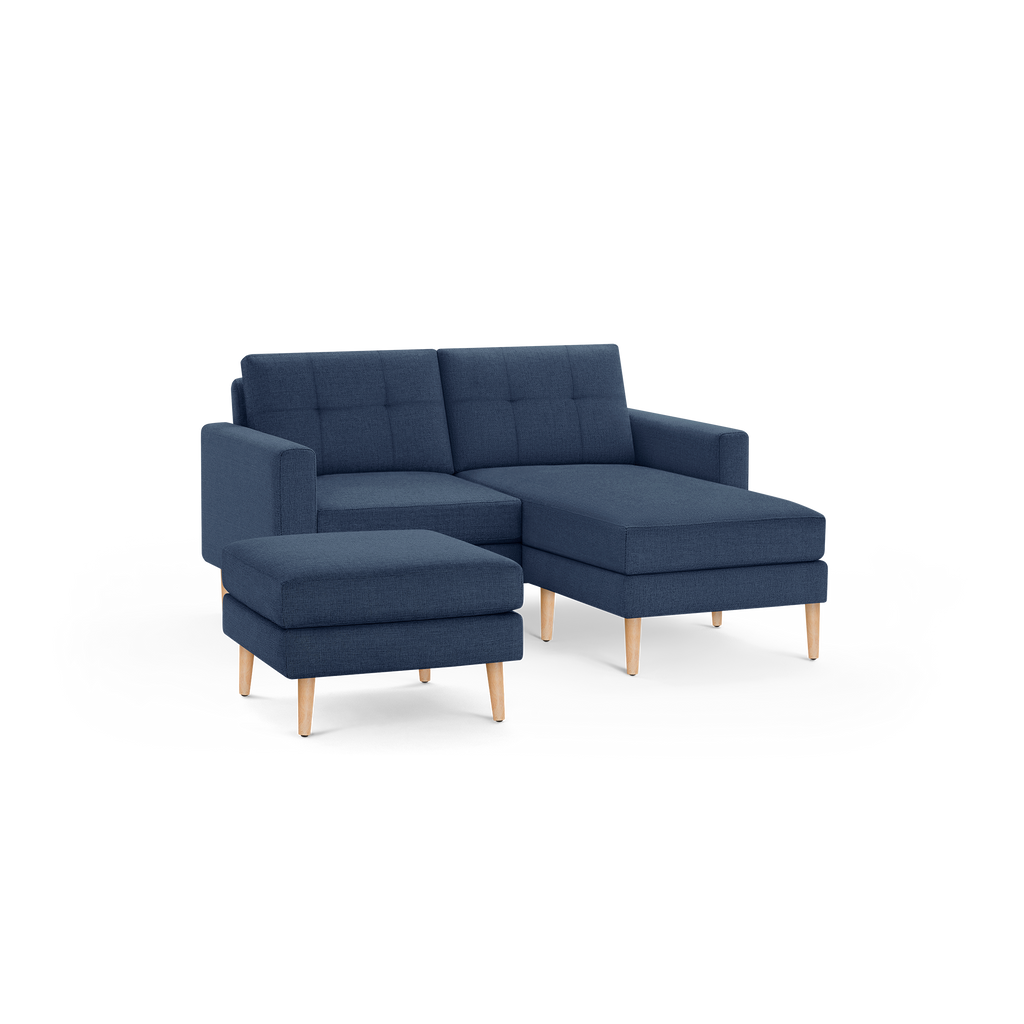 Modern navy blue fabric sectional sofa with tufted back cushions and matching ottoman, supported by wooden legs.