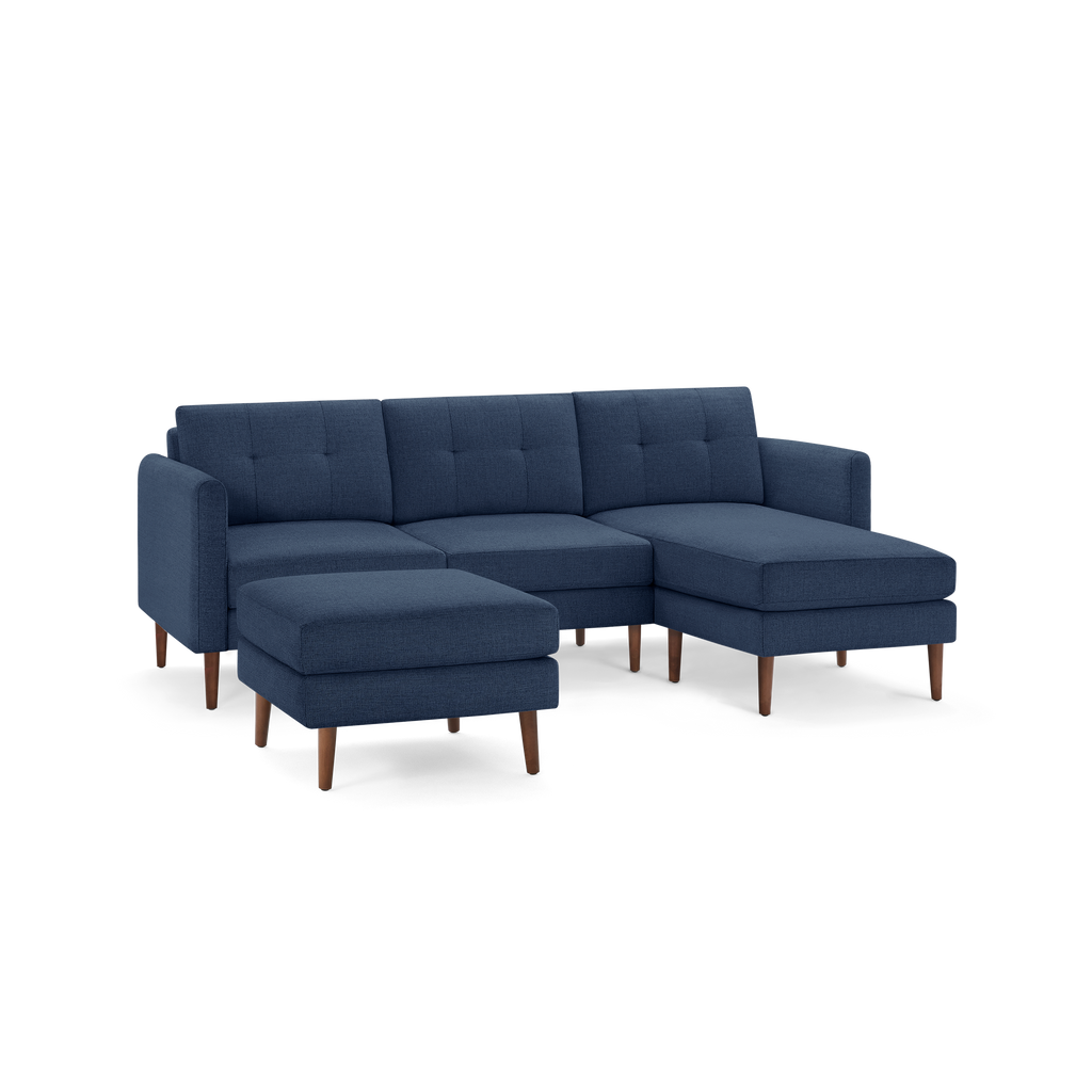 Modern navy blue sectional sofa with tufted back cushions, wooden legs, and a matching ottoman for versatile seating.