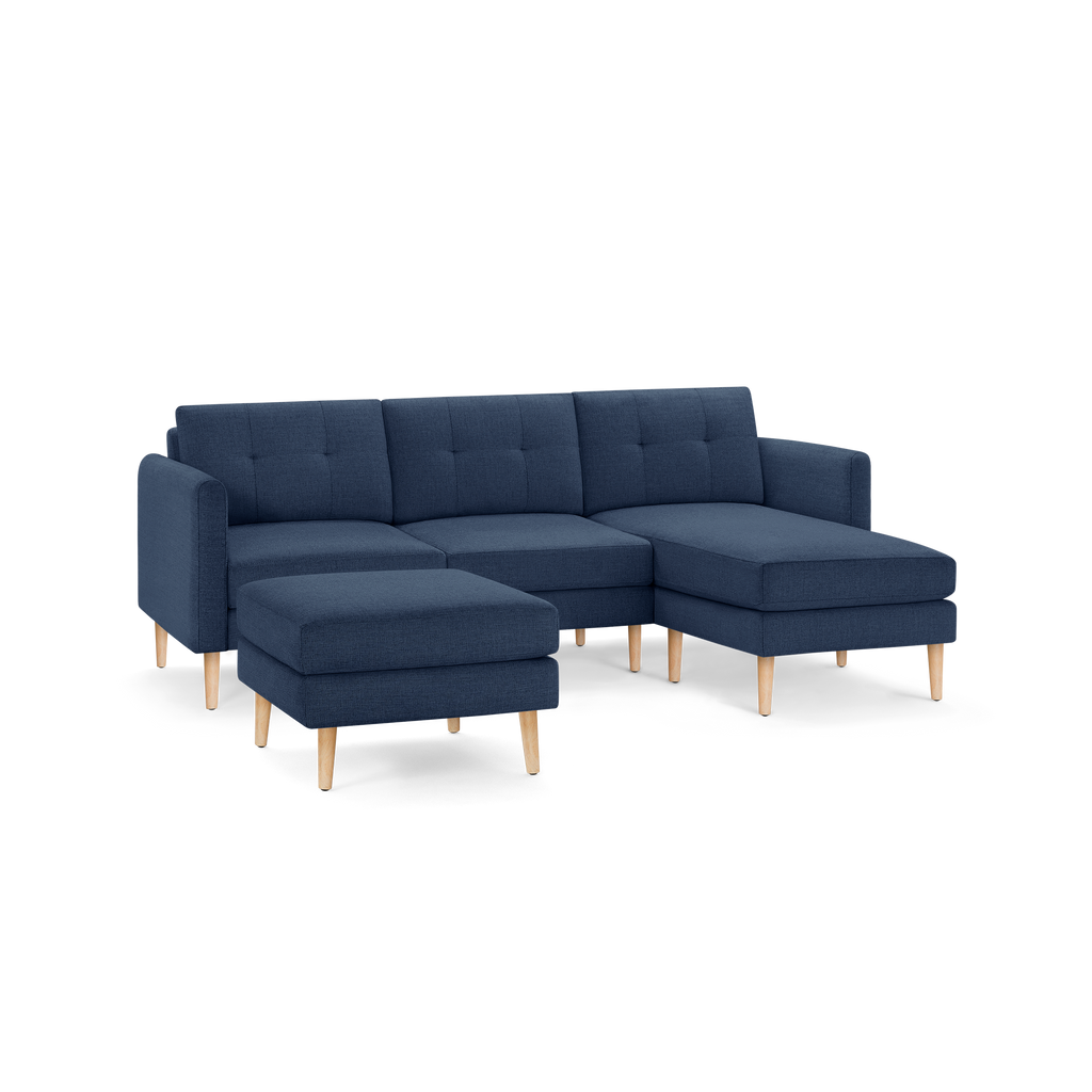 Modern navy blue fabric sectional sofa with tufted back cushions, wooden legs, and matching ottoman.