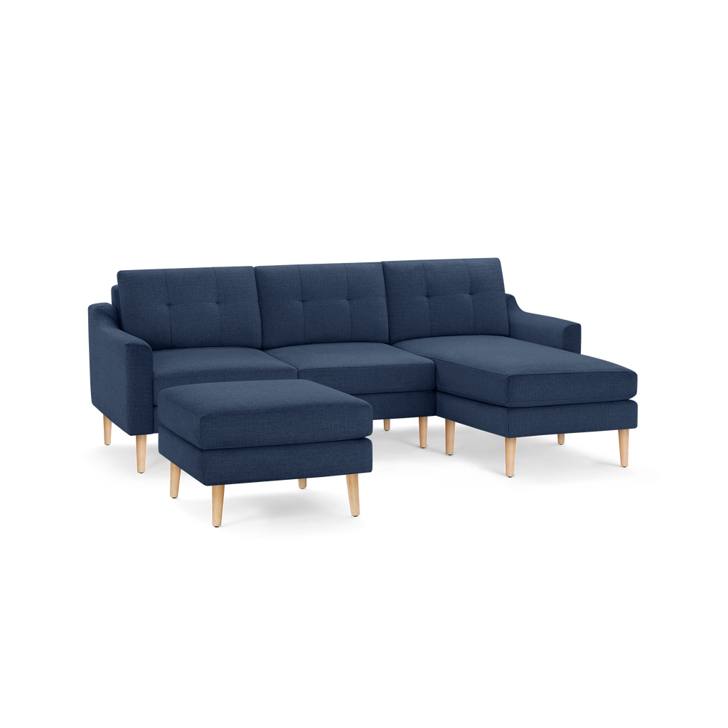 Modern navy blue fabric sectional sofa with wooden legs, tufted back cushions, and separate matching ottoman.