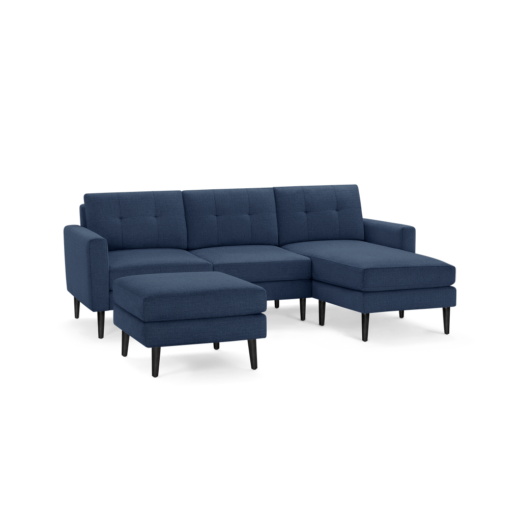 Modern navy blue fabric sectional sofa with tufted back cushions, a chaise lounge on the right, and a matching ottoman with black tapered legs.