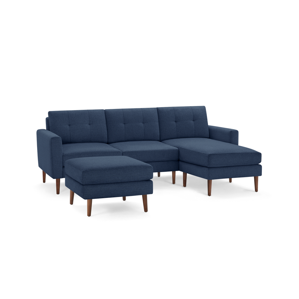 Modern navy blue sectional sofa with tufted back cushions, matching ottoman, and wooden tapered legs, offering comfortable seating.