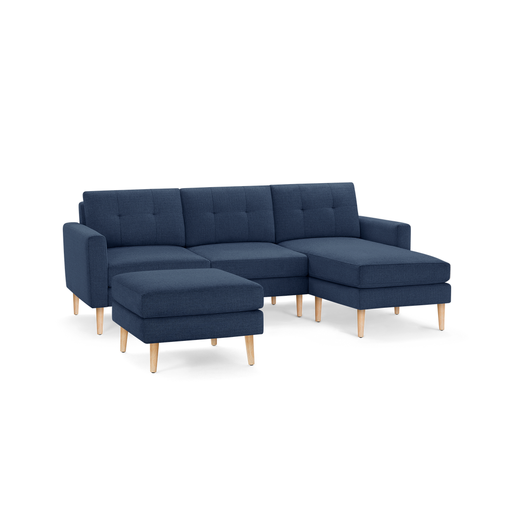 Modern navy blue sectional sofa with tufted cushions, wooden legs, and an attached chaise lounge and matching ottoman.