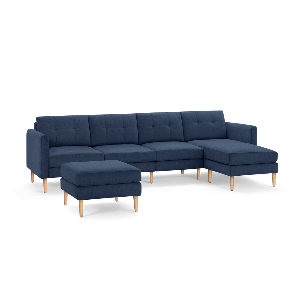 Dark blue modern sectional sofa with tufted back cushions and light wooden legs, featuring an ottoman and chaise lounge.