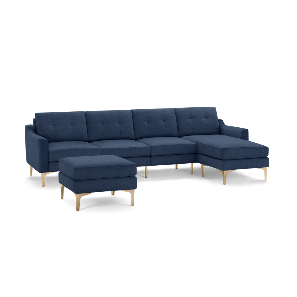Navy blue sectional sofa with tufted cushions, wooden legs, and matching ottoman, featuring a chaise lounge on the right side.