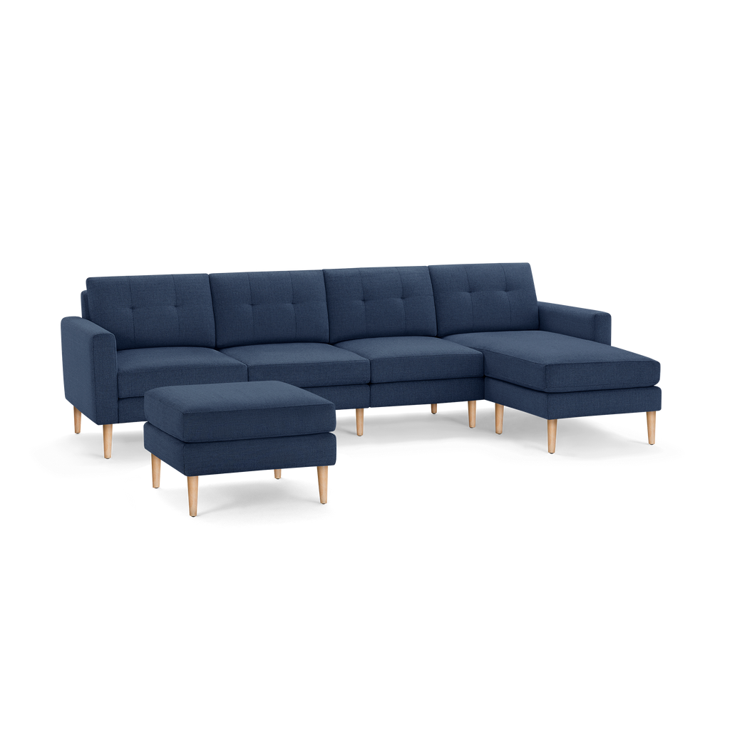 Blue fabric sectional sofa with wooden legs and matching ottoman, featuring tufted cushions and a right chaise lounge.