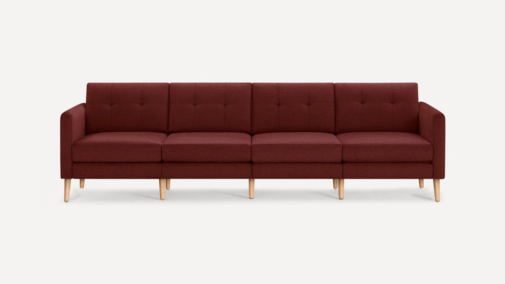 Modern four-seater sofa upholstered in dark red fabric with tufted back cushions and light wooden legs against a plain background.