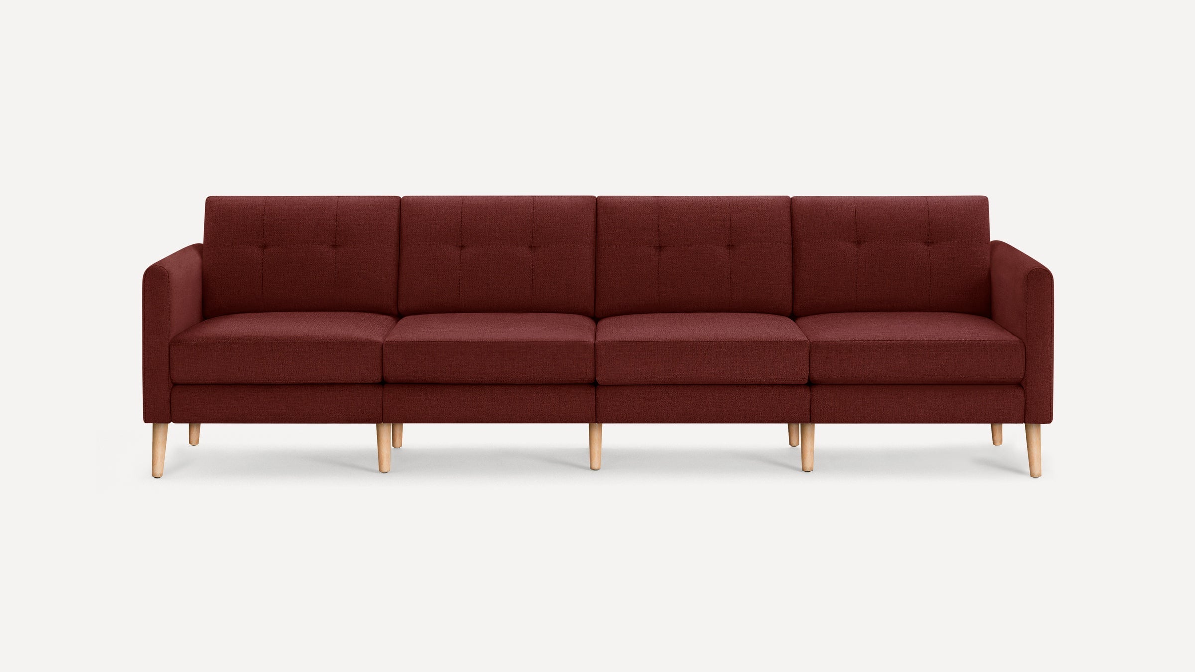 Modern four-seater sofa upholstered in dark red fabric with tufted back cushions and light wooden legs against a plain background.