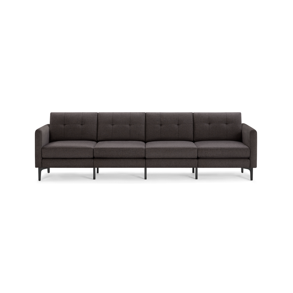 Modern dark gray fabric four-seater sofa with tufted cushions, straight armrests, and black metal legs against a transparent background.