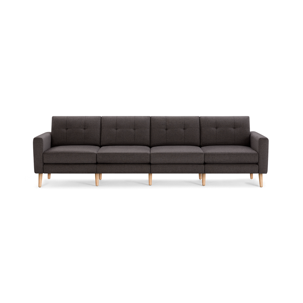 Dark gray modern four-seater sofa with tufted back cushions, straight armrests, and light wooden legs, isolated on black background.