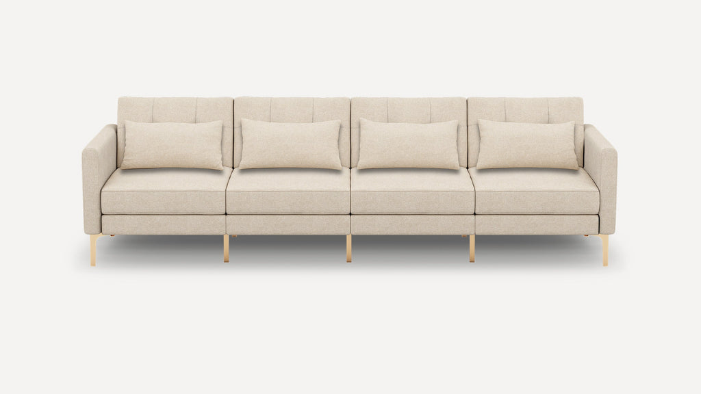 Four-seater beige fabric sofa with clean lines, vertical tufted backrests, gold metal legs, and four matching rectangular cushions.