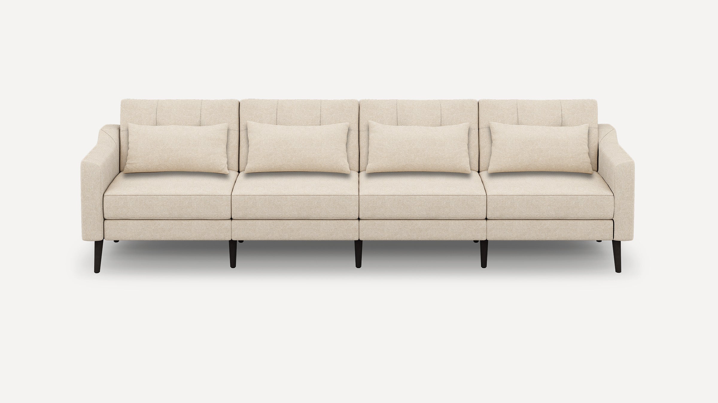 Beige modern four-seater sofa with clean lines, tufted back cushions, matching lumbar pillows, and dark wooden legs against white background.