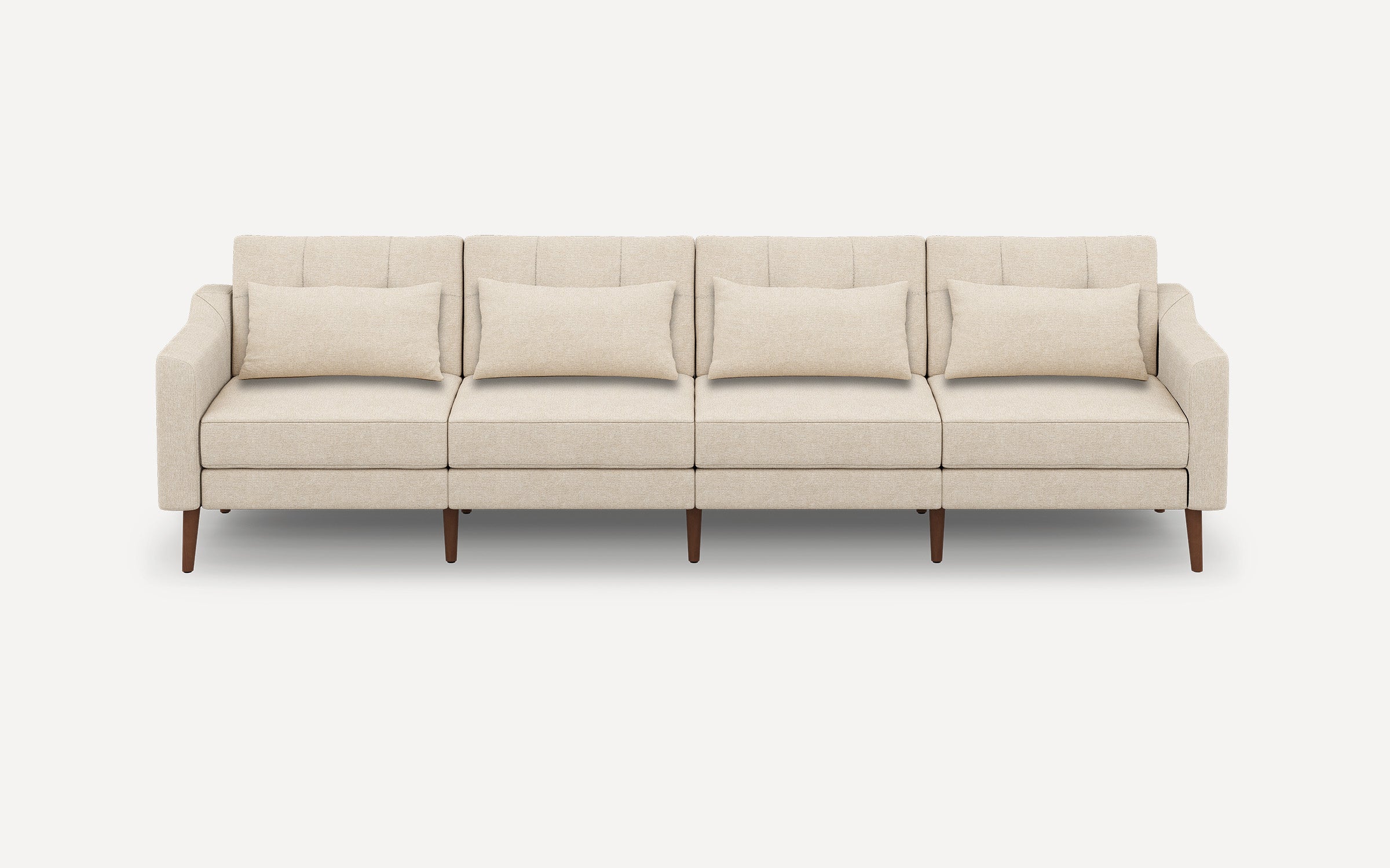 Modern four-seater beige fabric sofa with slim wooden legs, tufted back cushions, and matching rectangular throw pillows.