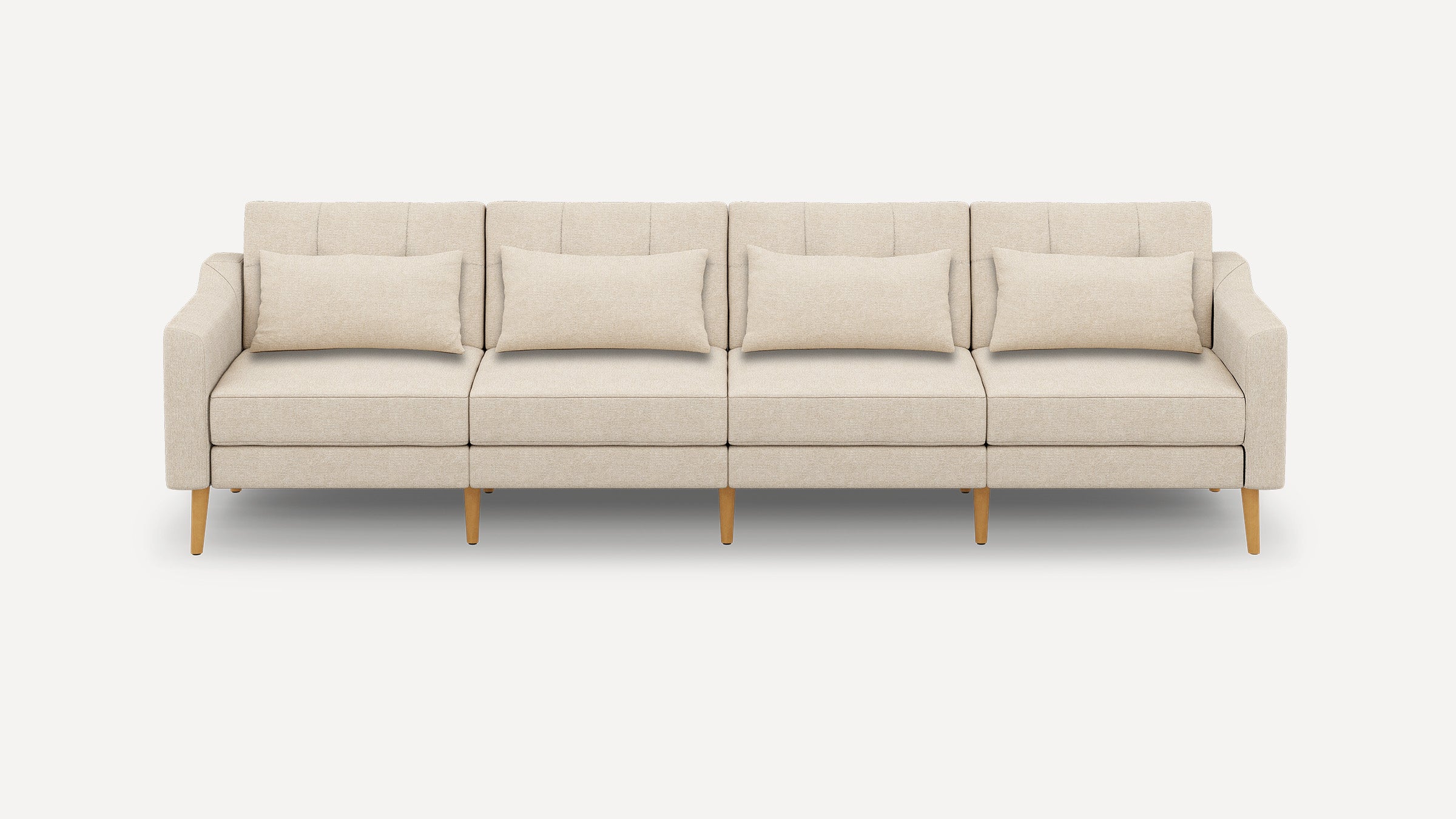 Four-seater beige fabric sofa with wooden legs, straight armrests, tufted back cushions, and four matching lumbar pillows.