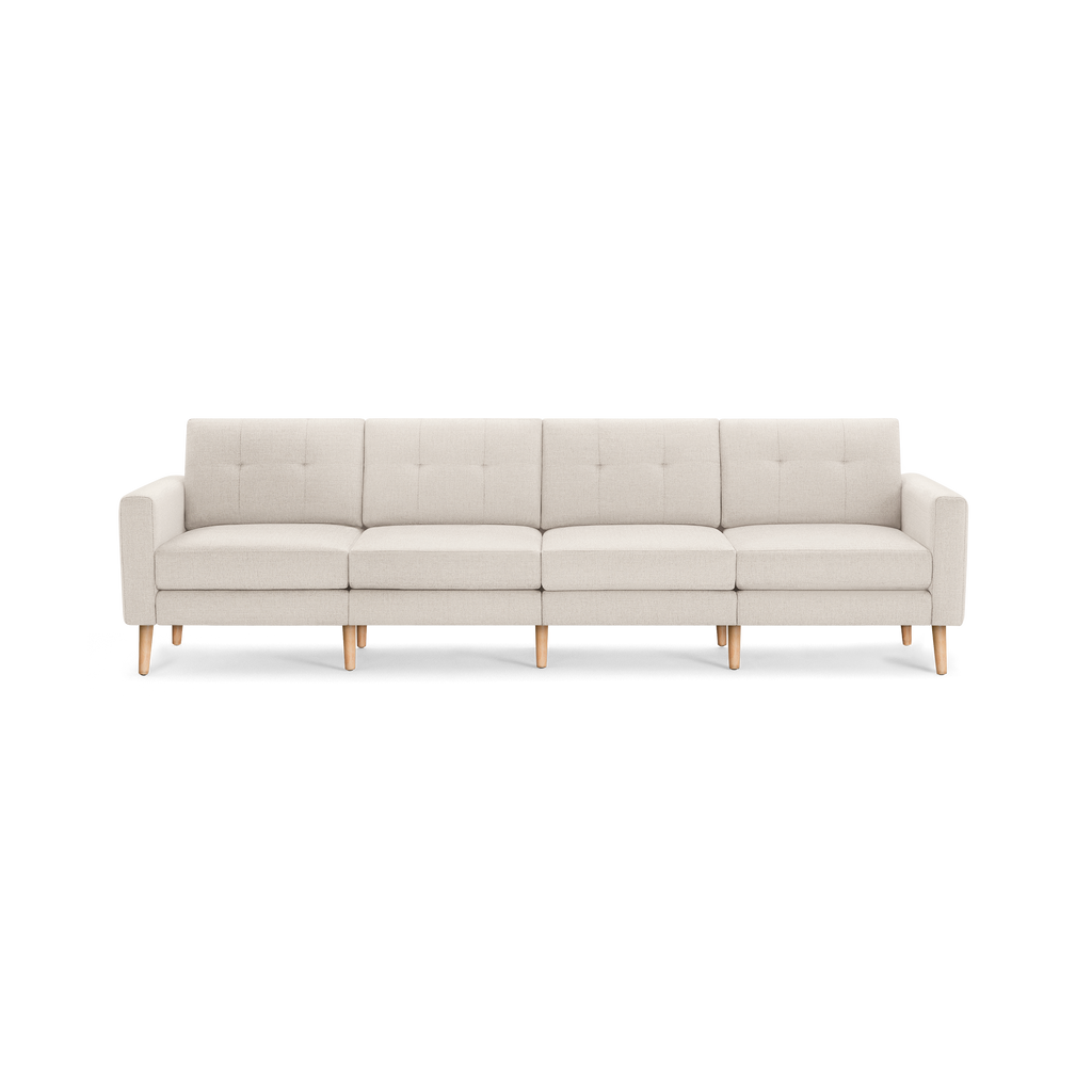 Cream-colored modern four-seat sofa with tufted back cushions and wooden legs on black background.