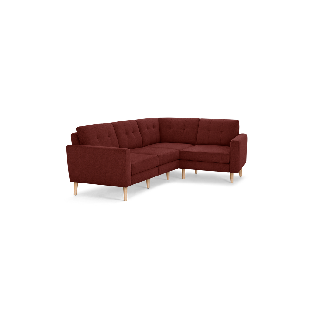 Modern L-shaped sectional sofa with tufted cushions, deep red fabric upholstery, and light wooden legs.