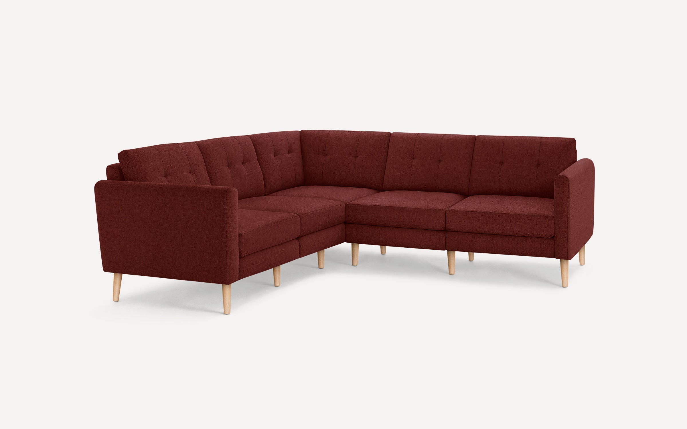 L-shaped sectional sofa upholstered in deep red fabric with tufted back cushions and light wooden legs, modern and cozy design.