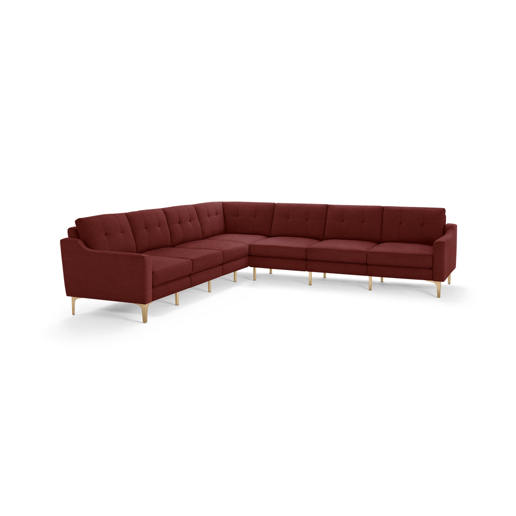 Large L-shaped sectional sofa with tufted backrest cushions, upholstered in dark red fabric, supported by light wood legs.