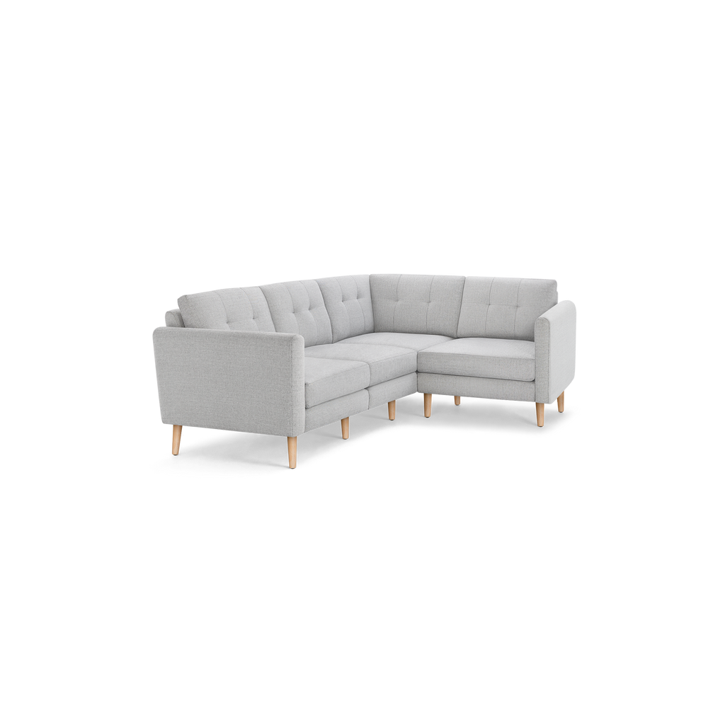 Light gray upholstered L-shaped sectional sofa with tufted back cushions and light wooden legs.