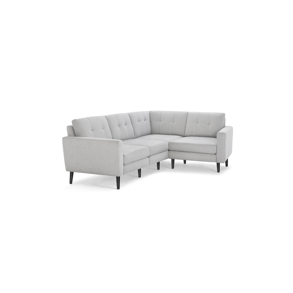 Light gray fabric L-shaped sectional sofa with tufted back cushions and slim dark wooden legs on black background.